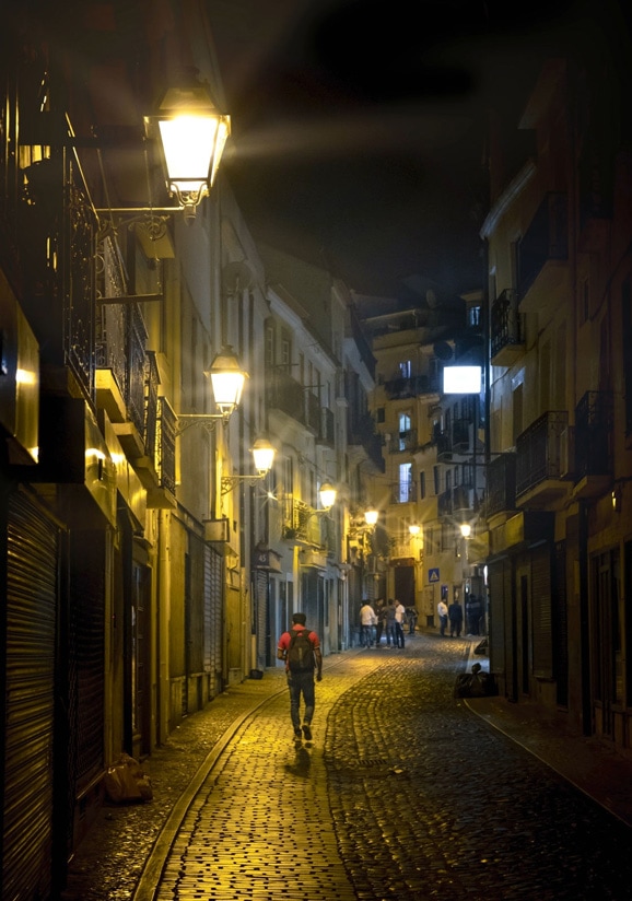 A man walking down the street with street lights glowing after Magic Light AI was applied
